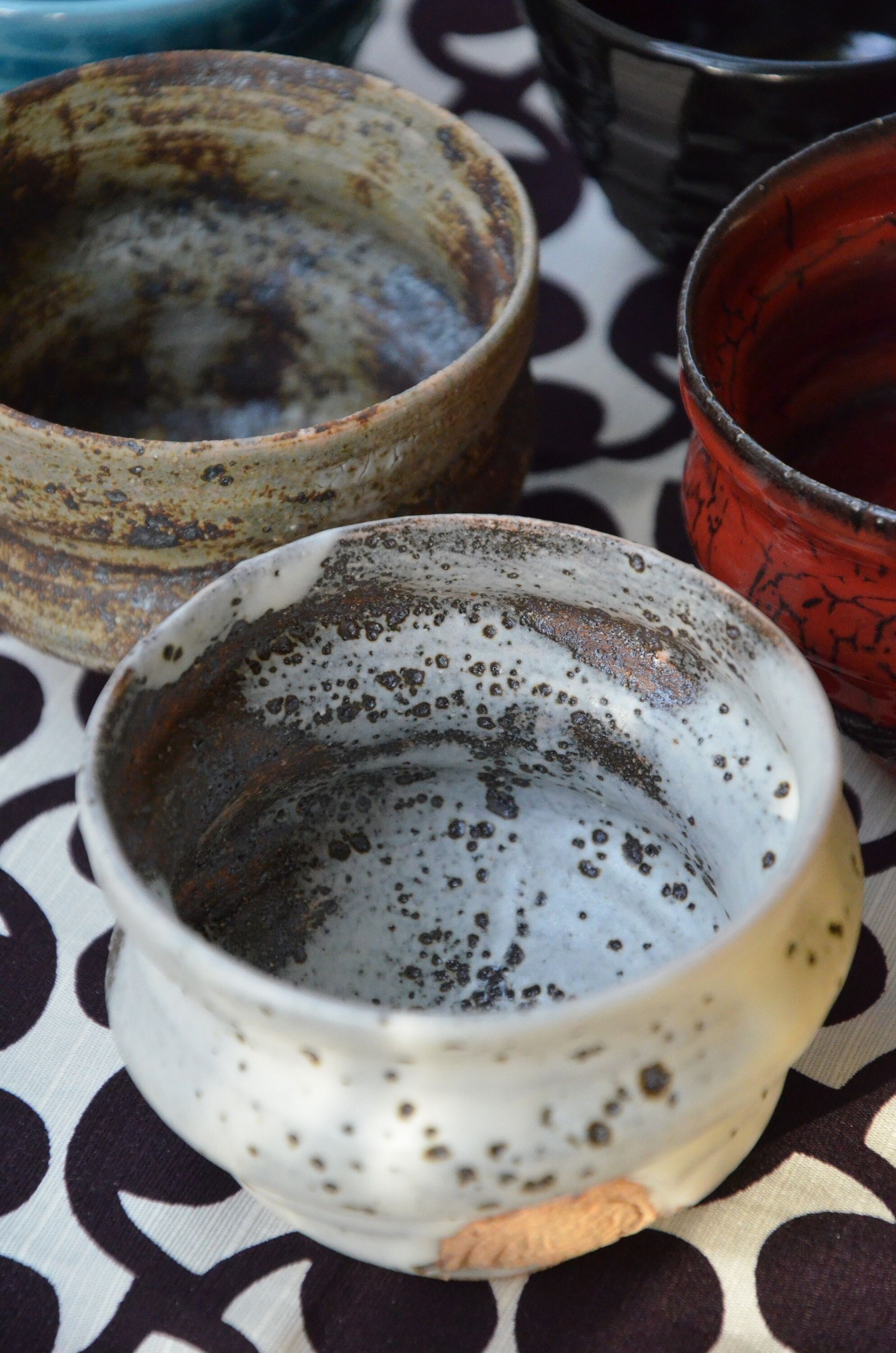 A close-up of two Ninshu ceramic cups, one white with dark stains and signs of wear inside, and another with a grey-brown patina. The inner surfaces show traces of use, with residue from beverages creating a natural, lived-in effect. The cloth underneath features a black polka-dot pattern on a white background, contrasting with the earthy tones of the cups.
