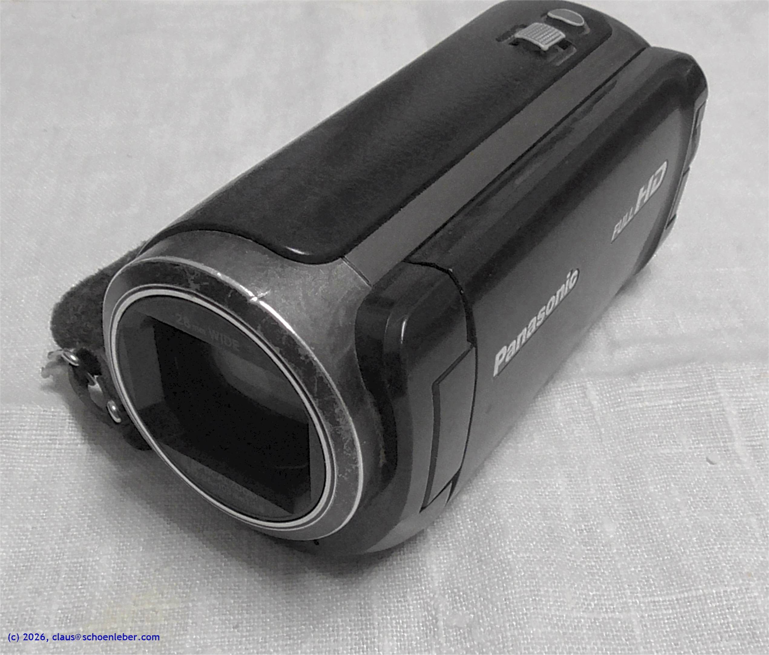 Abgebildet ist die angebotene Kamera Panasonic HC-W580, schwarz, gesehen con schräg oben, auf weiß-beigem Hintergrund.