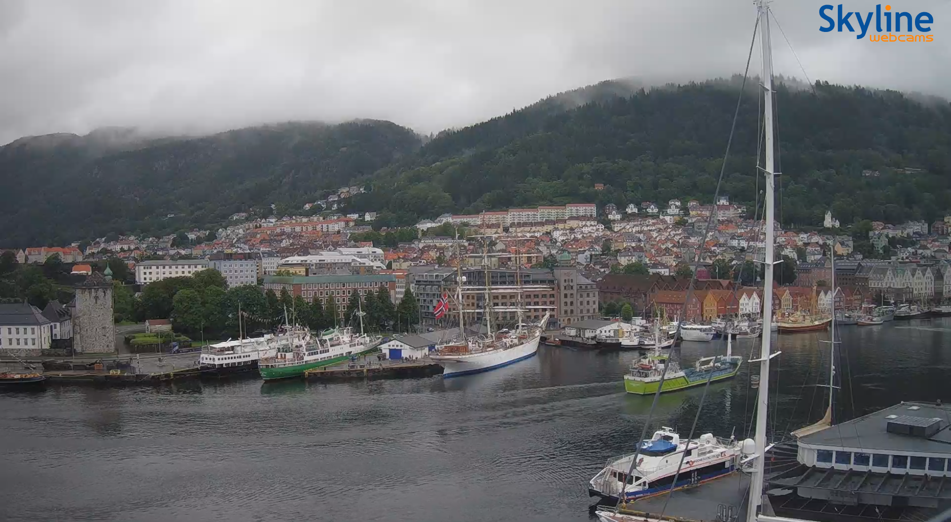 View from NODE office towards Bryggen, with old boats and ships gathering for Fjord Steam 2026. Clouds hang over the mountains surrounding the city.